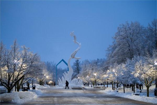  A person walks past a white art sculpture on a snowy university campus at dawn. 